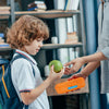 Profil eines braunhaarigen Jungen, in einem blauen Poloshirt, mit einem Rucksack auf dem Rücken. Er hält einen grünen Apfel in der rechten Hand, den er ansieht. Jemand anderes reicht ihm eine orangefarbene Brotdose. Auf der orangefarbenen Lunchbox befindet sich ein blauer Namensaufkleber, mit dem Namen Tom Parkinson in weißer School Print Schriftart.