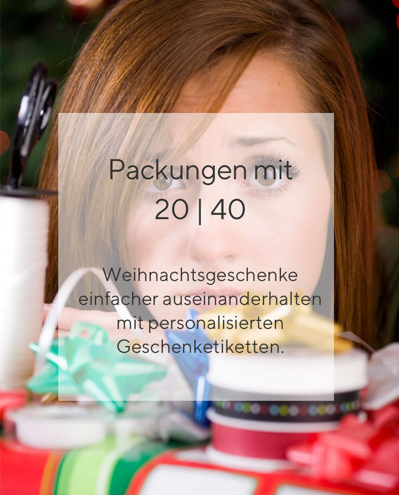 Ein Stapel mit sechs eingepackten Weihnachtsgeschenken, alle mit rot weißem Geschenkband versehen auf weißem Hintergrund. Im Vordergrund sind zwei rechteckige Weihnachtsgeschenkaufkleber zu sehen. Der obere ist dukelgrün, hat als Motiv drei Weihnachtsgeschenke abgebildet und einen Weihnachtsgruß der Familie Fischer. Der untere Weihnachtgeschenkaufkleber ist rot, bedruckt mit drei Tannenbäumen und einen Weihnachtsgruß der Firma Kuhn.