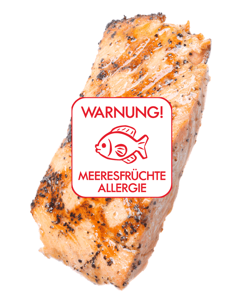 Ein Stück gegrillter Lachs mit einer glänzenden Pfefferglasur auf weißem Hintergrund. Auf dem Fisch befindet sich ein weißer Aufkleber mit einem Fischbild und rotem Text "Warnung - Meeresfrüchteallergie" in der Schriftart Clear und Simple.